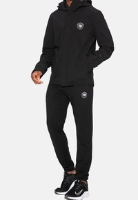 Schwarzer Sportanzug mit Reißverschluss-Kapuzenjacke und Logo sowie passenden Hosen mit Kordelzug-Bund und Logodetails.