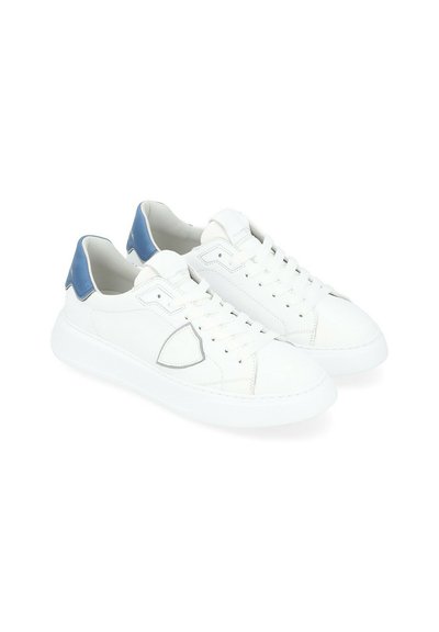 Sneakers bianchi con tomaia in pelle liscia, dettagli blu sul tallone e punta rotonda. Presentano chiusura con lacci e suola in gomma con cuciture sottili.