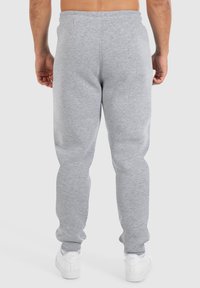 Pantalon de survêtement gris clair avec une taille élastique, des jambes fuselées et une texture douce. Porté avec des chaussures de sport blanches et sans poches visibles.