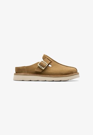 Chaussure en daim beige à enfiler avec bride boucle réglable et semelle en caoutchouc blanc, montrée de profil sur fond blanc.