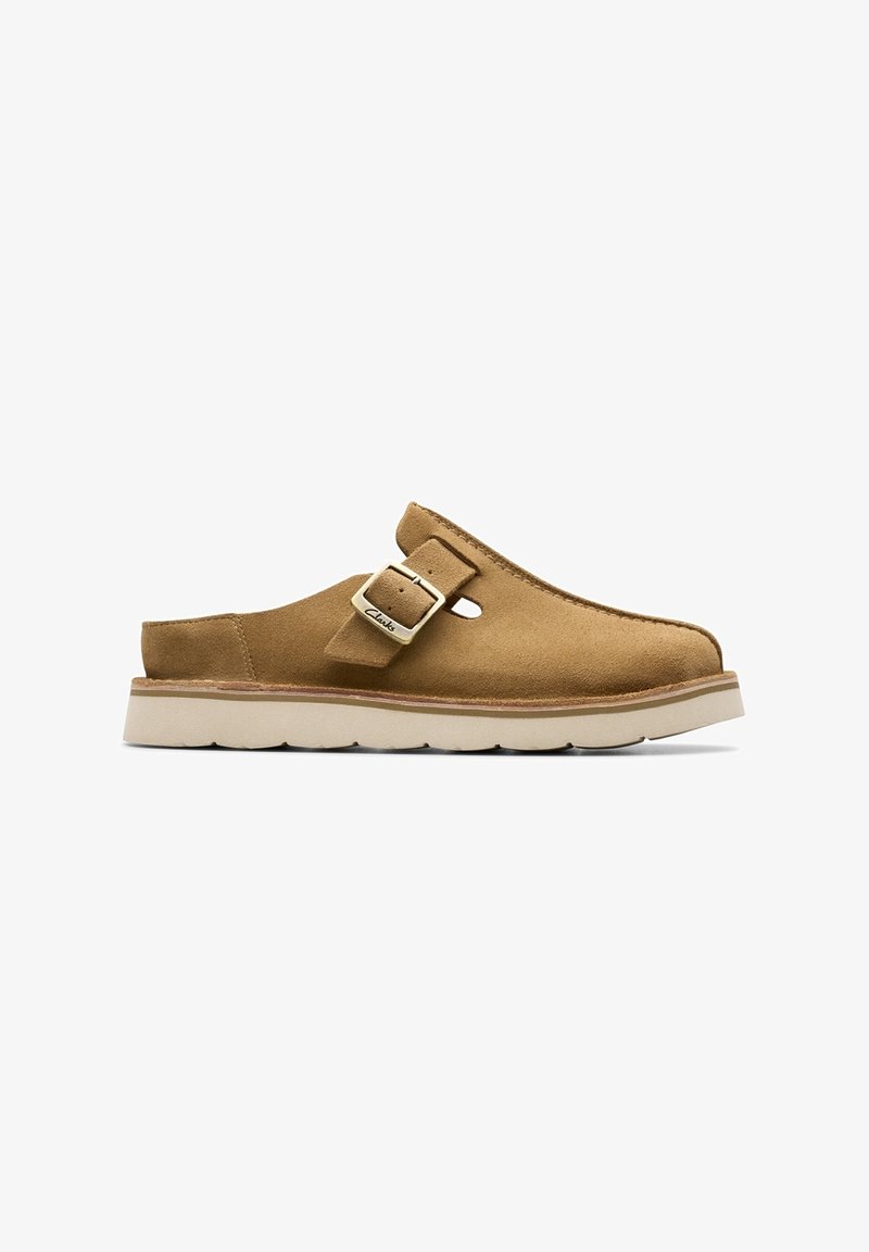 Chaussure en daim beige à enfiler avec bride boucle réglable et semelle en caoutchouc blanc, montrée de profil sur fond blanc.