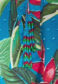 Farverigt stof med et blomstret mønster bestående af store blade og kronblade. Kanten er udsmykket med en dusksnore med perler i rødt, grønt og blåt.