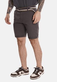 Shorts di cotone grigi con risvolti, accessori in metallo e una cintura a righe multicolori, indossati con scarpe sportive marroni e bianche.