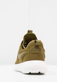 Nike-sneakers i olivgrönt tyg med vit sula. Har en rundad form, texturerat material och logotyp på hälen.