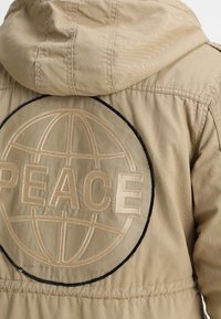 Kurtka khaki z kapturem, ozdobiona dużym okrągłym haftowanym wzorem z napisem "PEACE" i zarysem globu.