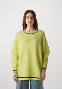 Sweater amarelo tricotado com design de logotipo em relevo, gola e punhos canelados pretos, e um corte oversized. Tecido macio e texturizado.
