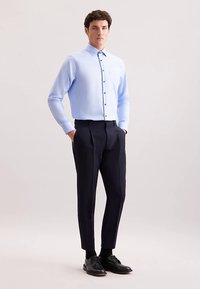 Jasnoniebieska koszula z długim rękawem i kołnierzykiem zapinanym na guziki, zestawiona z ciemnymi, dopasowanymi spodniami oraz czarnymi eleganckimi butami.