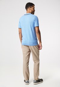 Modrá texturovaná polo košile s krátkými rukávy, spárovaná s světle béžovými kalhotami a černými teniskami. Polo má kontrastní límec.