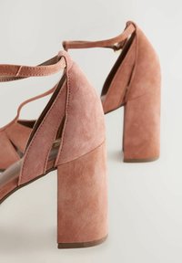Sandales à talons hauts en cuir suédé rose avec un design découpé, large talon bloc et brides à la cheville. Présente une texture lisse et une couleur solide.
