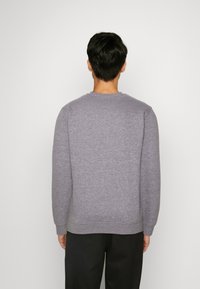 Felpa grigia con maniche lunghe e scollatura rotonda, realizzata in materiale morbido, con polsini e orlo a costine, indossata con pantaloni neri.