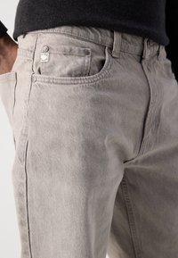 Hallid denim teksad klassikalise viiega tasku kujundusega, metallist nupuga ja peente õmblusdetailidega kitsas lõikes.