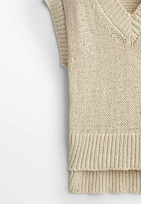 Veste en tricot beige avec col en V, manches courtes, ourlet côtelé et motif texturé. Le tissu semble doux et ample.