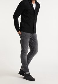 Cardigan nero lavorato a maglia con motivo a onde, dotato di colletto a scialle e chiusura con bottoni. Abbinato a jeans grigi e sneakers alte nere.