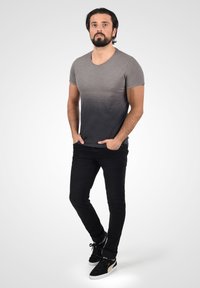Grå gradient T-shirt med korte ærmer, der går fra lys til mørk, parret med sorte jeans og sorte sneakers.