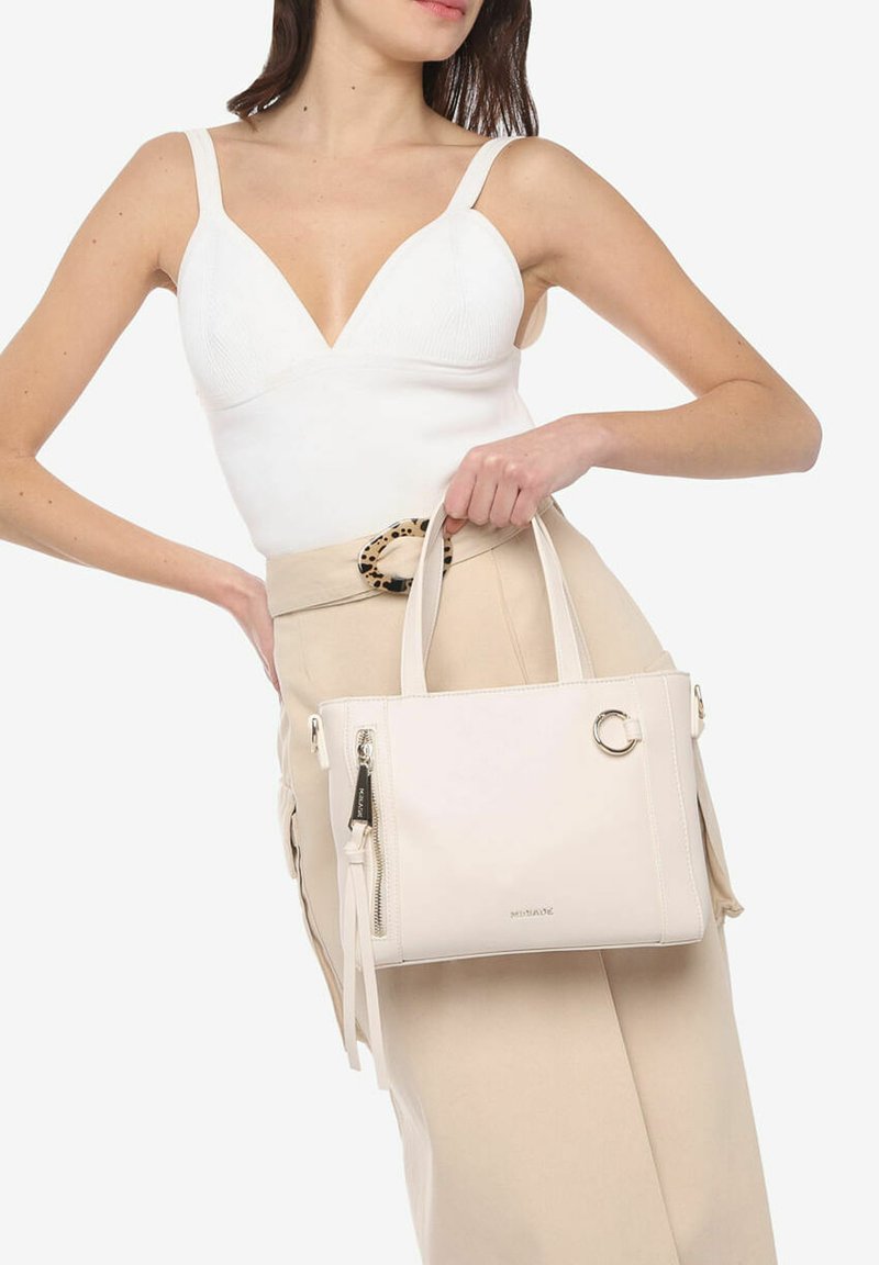 Witte leren handtas met dubbele handvatten, ritscompartimenten en een cirkelvormige hardware-accent. Glad textuur en minimalistisch ontwerp.