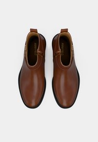 Bruine leren enkellaarsjes met een gladde afwerking, ronde neus en zwarte rubberen zool; beschikt over een ritssluiting en een achterste trekband.