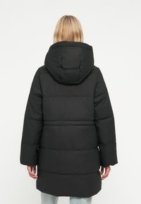 Čierna puferová bunda s kapucňou, dlhými rukávmi a prešívaným dizajnom s horizontálnymi sekciami. Bunda má uvoľnený strih a dĺžku po stred stehien.