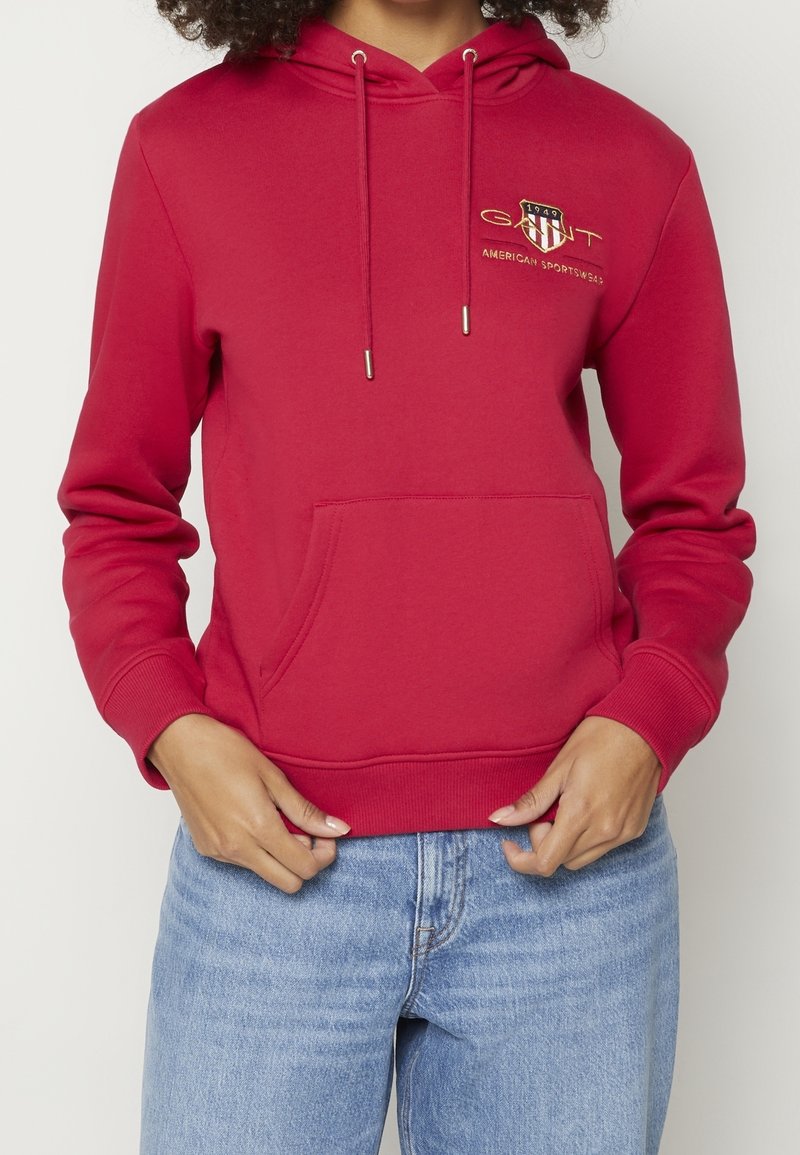 Czerwona bluza z kapturem, przednią kieszenią, ściągaczem w kapturze i haftowanym logo. Wykonana z miękkiego materiału, z ściągaczami na mankietach i w pasie.