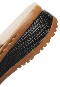 Close-up af brun og sort skosål med tekstureret sort greb og polstret lys beige inderforing.