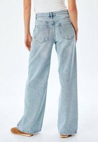Jeans de mezclilla de pernera ancha en azul claro, con una cintura alta, dos bolsillos traseros y una textura ligeramente desgastada.