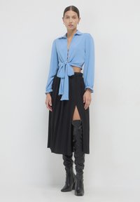 Cropped top azzurro chiaro a maniche lunghe con bottoni e allacciatura frontale; gonna nera plissettata con spacco alto; stivali neri lucidi fino al ginocchio.