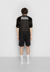 Black mesh short-sleeve shirt with glossy detailing. Features "VENOM" logo on the upper back. Paired with black shorts and white high-top sneakers.