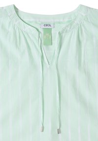 Blouse à rayures verticales vert clair et blanc avec un col rond, une fente en V à l'avant et des liens coulissants avec embouts métalliques.