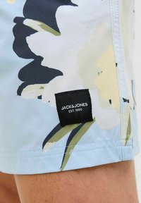 Világoskék fürdőnadrág nagy virágmintákkal, tengerészkék, zöld és sárga színekben. Fekete szövetcímke található rajta, amelyen az áll: "JACK & JONES EST. 1990."