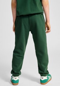 Grüne Jogginghose mit lockerer Passform, aus weichem Material gefertigt. Ein Paar grüne und weiße Sneaker mit braunen Gummisohlen, die unten sichtbar sind.