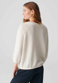 Weißer strukturierter Pullover mit 3/4-Ärmeln, im lockeren Schnitt und mit rundem Ausschnitt, kombiniert mit dunkelblauen Hosen.