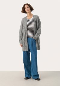 Cardigan lung gri, realizat dintr-un tricot moale, purtat peste o cămașă cu dungi alb-negru. Combinație cu pantaloni largi bleu deschis și pantofi negri.