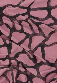 Ροζ ύφασμα με μαύρο ακανόνιστο σχέδιο που μοιάζει με καμηλοπάρδαλη, εμφανίζοντας φυσικές πτυχώσεις και υφή.