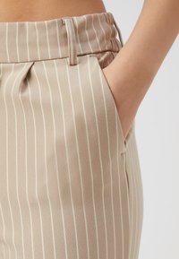 Beige gestreepte broek met een getailleerde pasvorm, voorzien van verticale witte strepen, een vlakke tailleband en zijzakken voor praktische doeleinden.