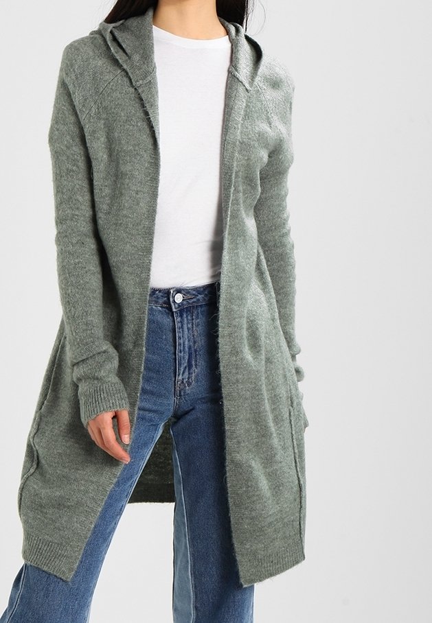 Lång grön cardigan med huva, tillverkad av mjukt material. Har ribbade muddar och öppen front, bärs över en vit skjorta och blå jeans.