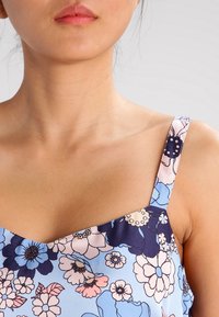 Blomsterprint top med en lyseblå baggrund, prydet med flerfarvede blomster i pink, marineblå og hvid. Tynde stropper og kvadratisk halsudskæring.