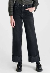 Jean noir à jambes larges en denim, avec une taille haute, des ourlets retroussés et des poches avant. Texture lisse avec des détails de couture minimaux.