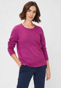 Fuchsia pullover trui met horizontale ribbelstructuur, ronde hals en lange mouwen, gecombineerd met donkerblauwe broek.