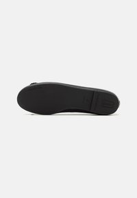 Zapato plano negro con una parte superior de cuero liso y puntera redondeada. La suela es plana y está hecha de goma, con una marca en relieve en el talón.