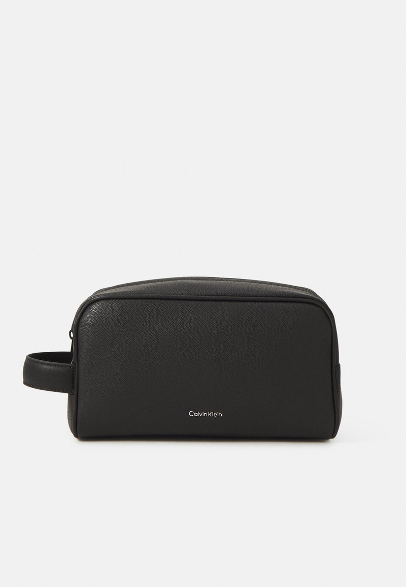 Svart lær toilettveske med rektangulær form, glatt tekstur, glidelås-lukking og sidehåndtak. Har en sølvfarget "Calvin Klein"-logo.
