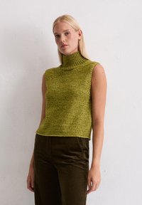 Groene gebreide mouwloze sweater met een hoge ribbelboord en een textuurafwerking, gecombineerd met eenbruine corduroy broek. Soepele en strakke pasvorm.