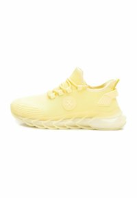 Zapatillas deportivas de color amarillo claro con una parte superior de malla transpirable, que presentan un logo redondo, acentos texturizados y una suela gruesa y ondulada.