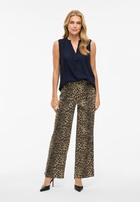 Blusa sin mangas de color azul marino con escote en V, combinada con pantalones de pierna ancha de estampado de leopardo en tonos marrón y negro. Los zapatos son tacones negros de punta.