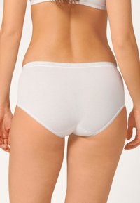 Mutande bianche di cotone con una texture liscia, design a vita bassa e delicata rifinitura a picot, viste da dietro.