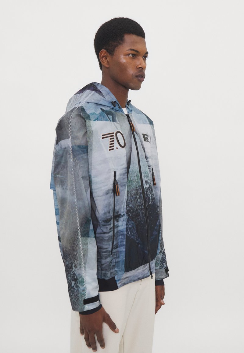 Leichte, kapuzenjacke mit einem blauen und grauen abstrakten Muster, Reißverschluss und schwarzen Rippenbündchen. Auffällige orangefarbene Akzentreißverschlüsse.