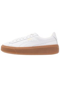 Zapatillas de cuero blancas con suela de goma, cordones planos y detalles de costura sutiles. Presenta un logo dorado en el lateral. Diseño clásico de tipo low-top.