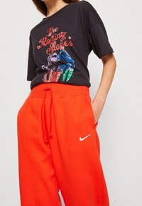 Black t-shirt features "The Rolling Stones" graphic with colorful lips design. Paired with bright orange Nike sweatpants, featuring a white logo.