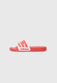 Sarkanie Adidas slaidu čības ar baltu siksnu, uz kuras ir izteikts sarkanais logotips un trīs svītras. Gluda tekstūra un plakana zole.