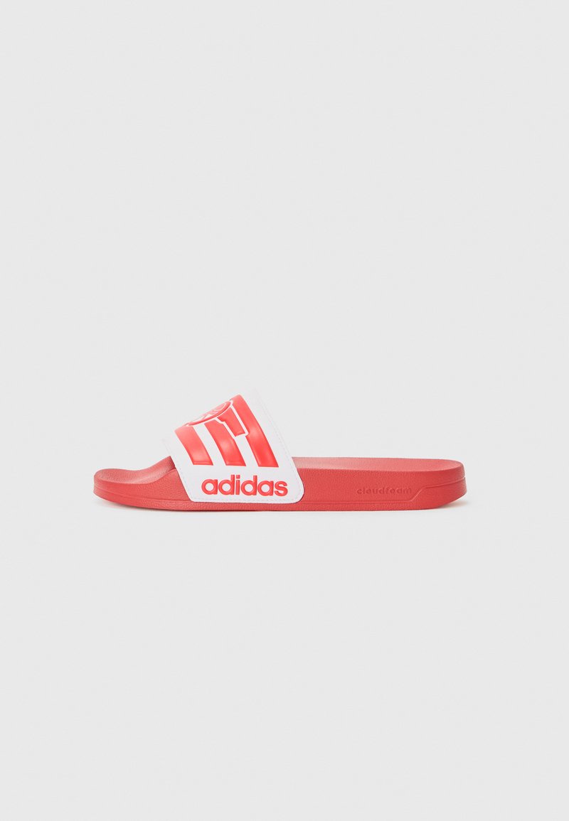 Sarkanie Adidas slaidu čības ar baltu siksnu, uz kuras ir izteikts sarkanais logotips un trīs svītras. Gluda tekstūra un plakana zole.