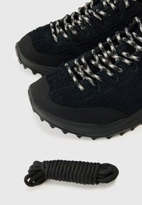 Čierne športové topánky s textúrovaným čiernym zvrškom, spevnenou špičkou, šnúrkami so strieborno-čiernym vzorom a čiernou šnúrkou vedľa nich.