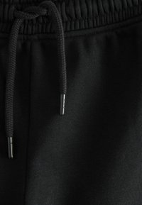 Schwarzer Sweatpants-Stoff mit glatter Textur. Elastischer Bund mit Kordelzug, ausgestattet mit schwarzen Aglets. Einfaches und minimalistisches Design.